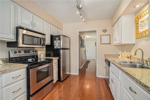 kitchen featuring appliances with stainless steel finishes, white cabinetry, sink, light hardwood / wood-style floors, and a textured ceiling