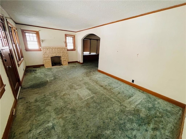 unfurnished living room with crown molding, a stone fireplace, a textured ceiling, and dark carpet