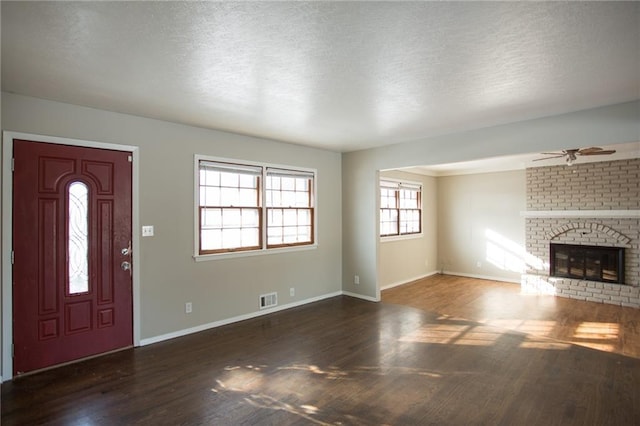 unfurnished living room with a brick fireplace, dark wood-type flooring, a textured ceiling, and ceiling fan