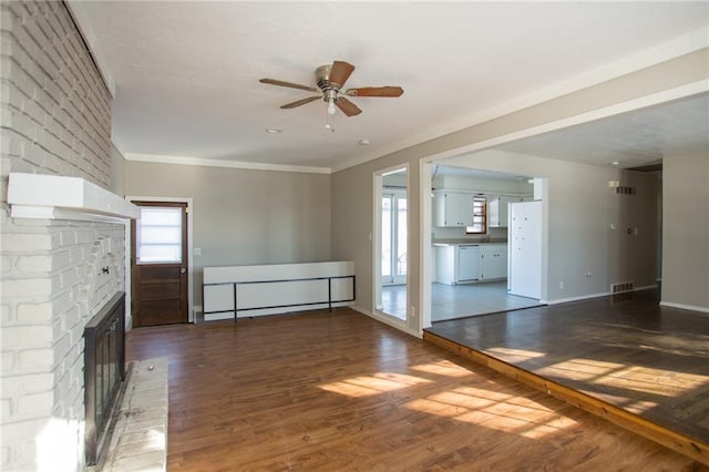 unfurnished living room featuring a brick fireplace, dark hardwood / wood-style flooring, ornamental molding, and ceiling fan