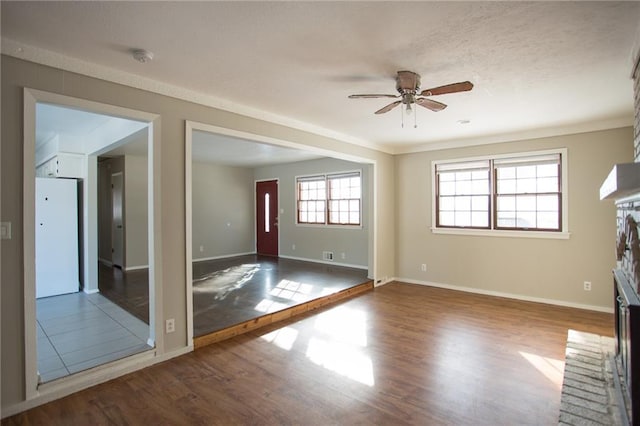 interior space with dark wood-type flooring, a brick fireplace, ornamental molding, and ceiling fan