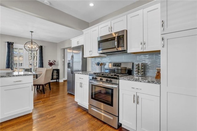 kitchen with stainless steel appliances, wood-type flooring, white cabinets, and backsplash