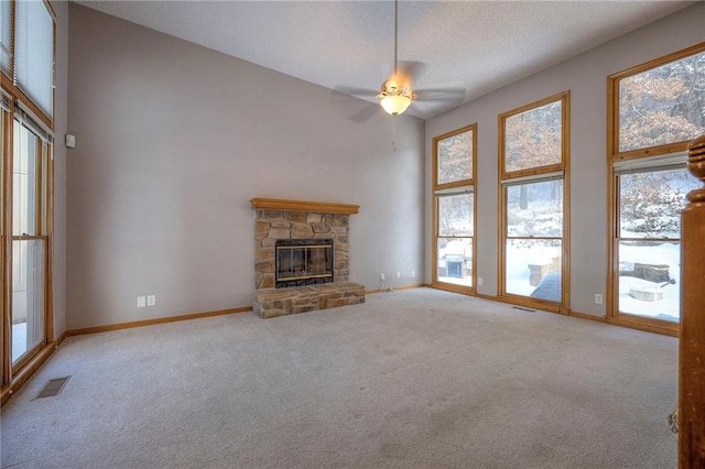 unfurnished living room with a towering ceiling, light colored carpet, ceiling fan, and a stone fireplace