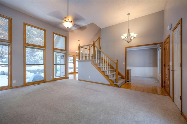 unfurnished living room featuring high vaulted ceiling, light carpet, and an inviting chandelier