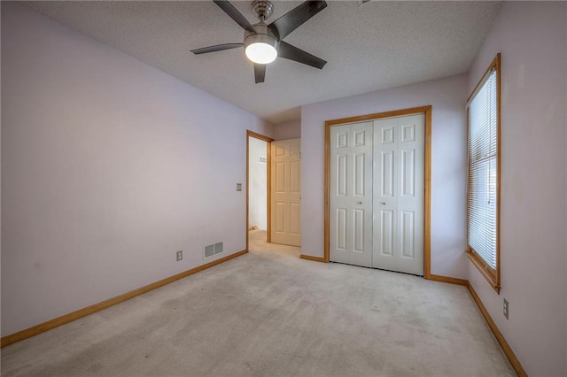 unfurnished bedroom featuring a closet, ceiling fan, a textured ceiling, and light carpet