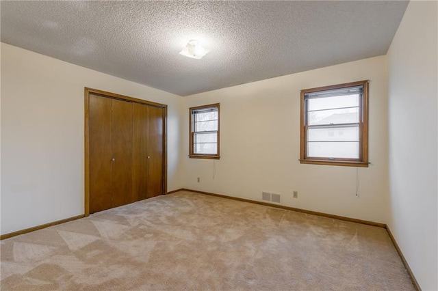 unfurnished bedroom with light colored carpet, a closet, and a textured ceiling