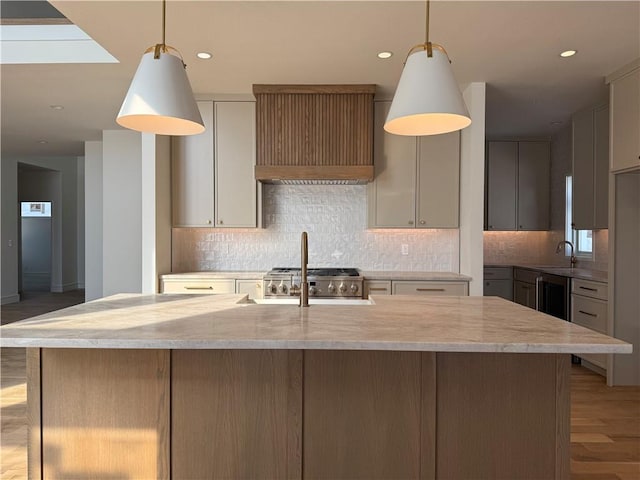 kitchen with custom exhaust hood, a kitchen island with sink, pendant lighting, and light wood-type flooring