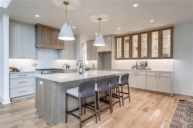 kitchen featuring white cabinetry, decorative light fixtures, light hardwood / wood-style floors, and a center island with sink