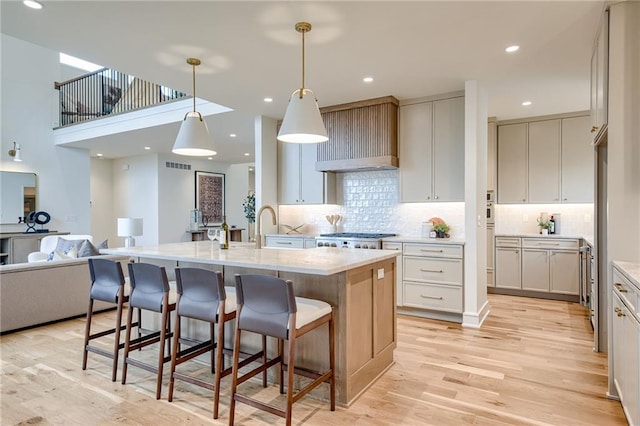 kitchen with stove, hanging light fixtures, a center island with sink, and light hardwood / wood-style flooring