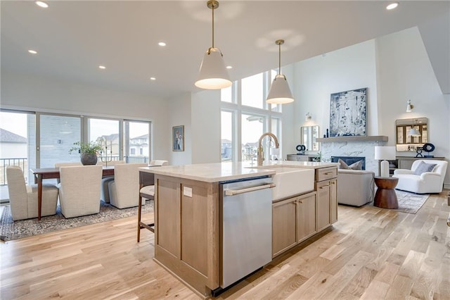 kitchen with sink, decorative light fixtures, light hardwood / wood-style flooring, stainless steel dishwasher, and an island with sink