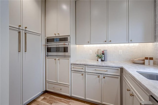 kitchen featuring backsplash, light stone countertops, stainless steel oven, and light wood-type flooring