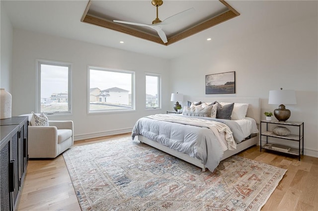 bedroom featuring a tray ceiling, ceiling fan, and light wood-type flooring