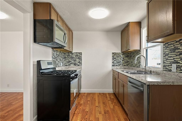 kitchen with sink, tasteful backsplash, a textured ceiling, appliances with stainless steel finishes, and light hardwood / wood-style floors