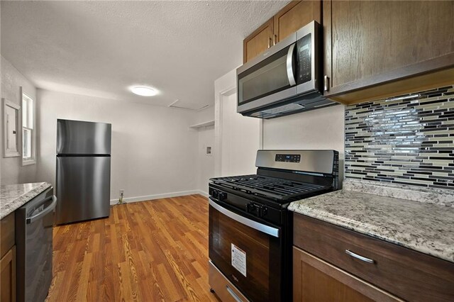 kitchen featuring stainless steel appliances, tasteful backsplash, light stone counters, and light hardwood / wood-style flooring