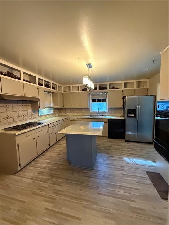 kitchen featuring a kitchen island, tasteful backsplash, hanging light fixtures, black appliances, and light hardwood / wood-style flooring