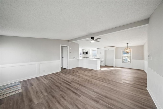 unfurnished living room featuring ceiling fan with notable chandelier, lofted ceiling with beams, dark hardwood / wood-style floors, and a textured ceiling