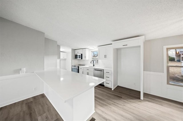 kitchen with light hardwood / wood-style flooring, stainless steel appliances, kitchen peninsula, and white cabinets