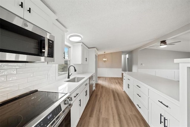 kitchen with appliances with stainless steel finishes, decorative light fixtures, white cabinetry, sink, and light hardwood / wood-style floors