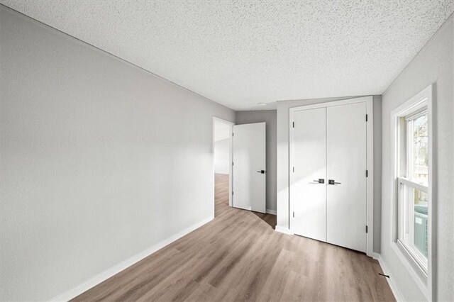 unfurnished bedroom with a textured ceiling, light hardwood / wood-style floors, and a closet