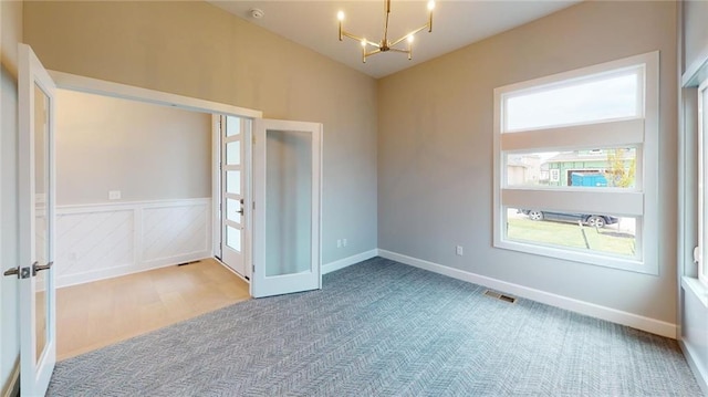 carpeted spare room featuring french doors, a notable chandelier, and vaulted ceiling