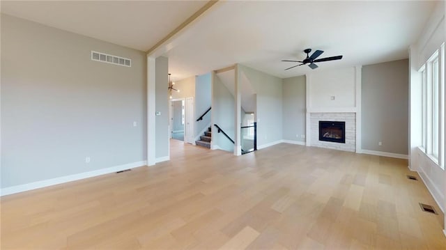 unfurnished living room with ceiling fan with notable chandelier, light hardwood / wood-style flooring, and a stone fireplace