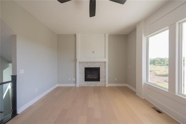 unfurnished living room featuring a brick fireplace, a wealth of natural light, light hardwood / wood-style floors, and ceiling fan