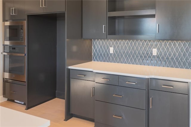 kitchen with backsplash, gray cabinets, oven, and built in microwave