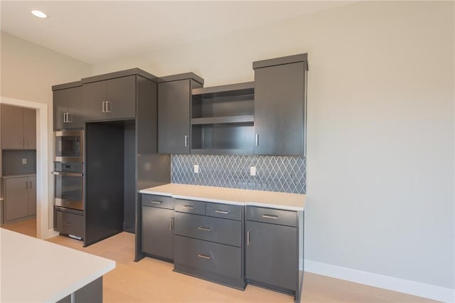 kitchen featuring tasteful backsplash, gray cabinets, oven, light wood-type flooring, and built in microwave