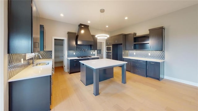 kitchen with exhaust hood, appliances with stainless steel finishes, decorative light fixtures, a kitchen island, and sink