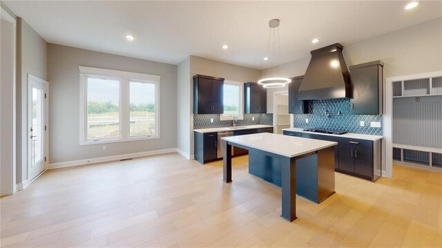 kitchen featuring decorative light fixtures, premium range hood, a kitchen island, sink, and a kitchen breakfast bar