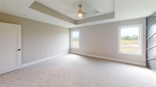 spare room featuring a raised ceiling, light carpet, and ceiling fan