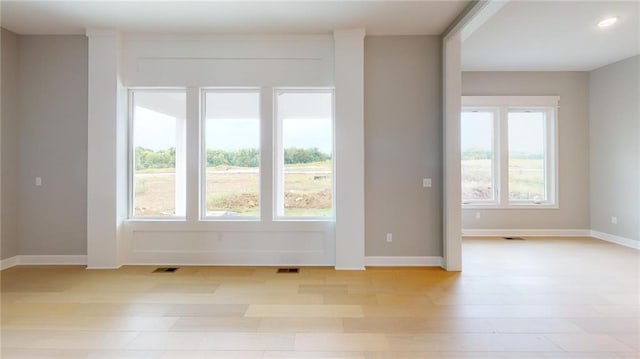 unfurnished room featuring baseboards, light wood finished floors, visible vents, and a healthy amount of sunlight