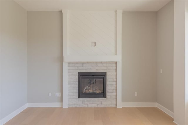 unfurnished living room featuring wood finished floors, a glass covered fireplace, and baseboards