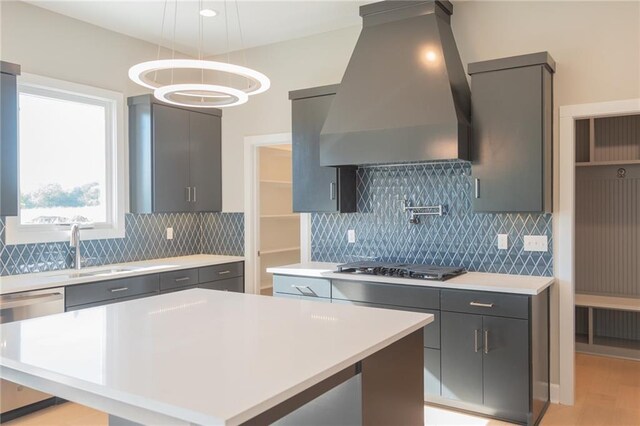 kitchen featuring stainless steel appliances, a sink, custom range hood, light countertops, and pendant lighting