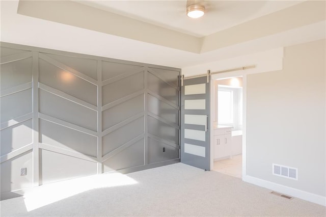 interior space featuring light carpet, a barn door, visible vents, and ensuite bathroom