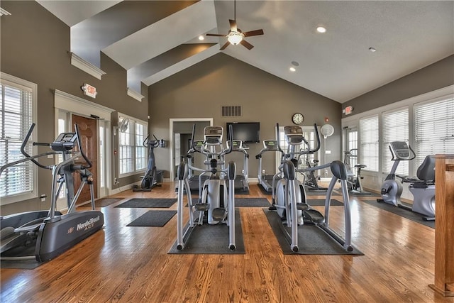 exercise room with high vaulted ceiling, plenty of natural light, wood finished floors, and visible vents