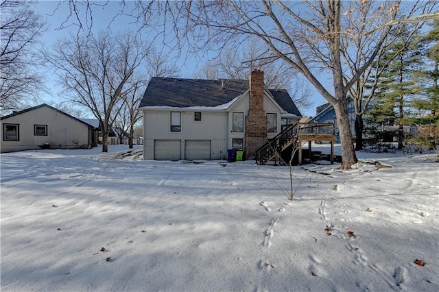 snow covered rear of property with a wooden deck and a garage