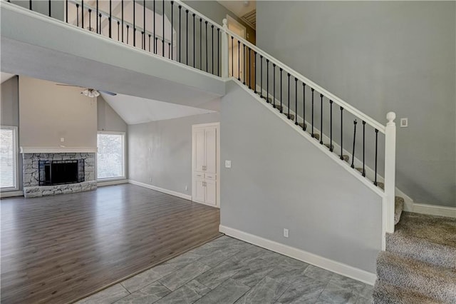 stairs with high vaulted ceiling, ceiling fan, a fireplace, and wood-type flooring