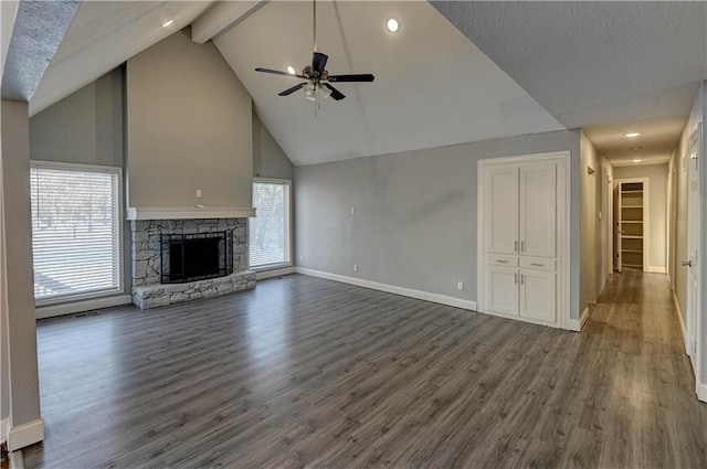 unfurnished living room with ceiling fan, dark hardwood / wood-style flooring, beamed ceiling, and a stone fireplace