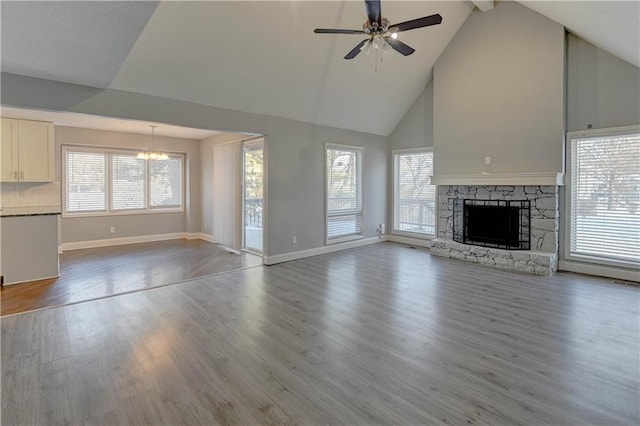 unfurnished living room with high vaulted ceiling, wood-type flooring, a fireplace, and ceiling fan with notable chandelier