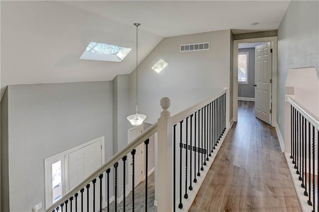 hall with lofted ceiling with skylight and light hardwood / wood-style flooring