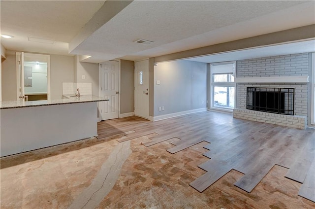 unfurnished living room featuring sink, a textured ceiling, light hardwood / wood-style flooring, and a fireplace