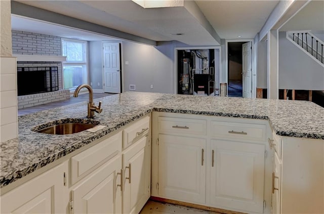 kitchen featuring kitchen peninsula, a fireplace, light stone countertops, white cabinets, and sink