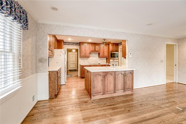 kitchen with light hardwood / wood-style floors, kitchen peninsula, white appliances, and crown molding