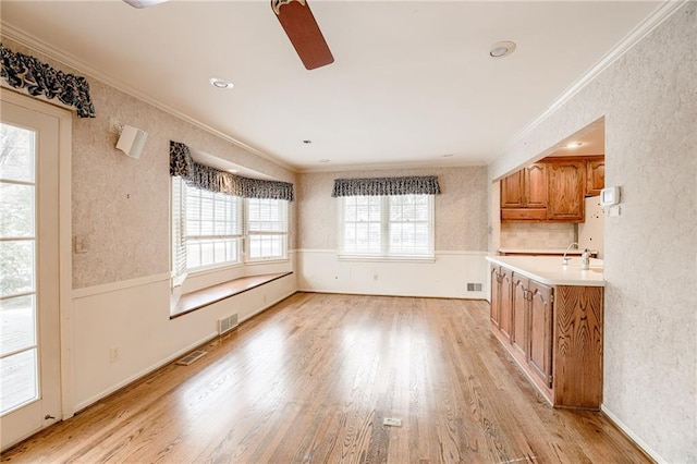 unfurnished dining area with ceiling fan, plenty of natural light, crown molding, and light wood-type flooring