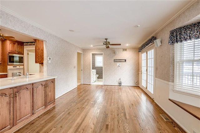 unfurnished living room featuring ceiling fan, light wood-type flooring, sink, and crown molding