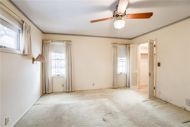 carpeted spare room with ceiling fan, a wealth of natural light, and crown molding