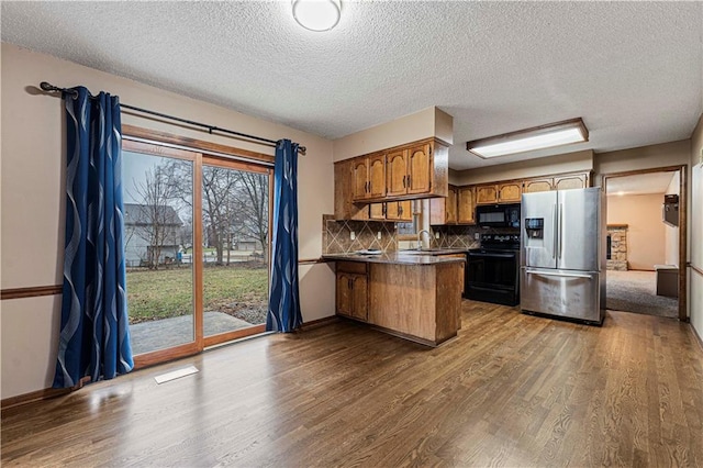 kitchen featuring a breakfast bar area, wood-type flooring, black appliances, decorative backsplash, and kitchen peninsula