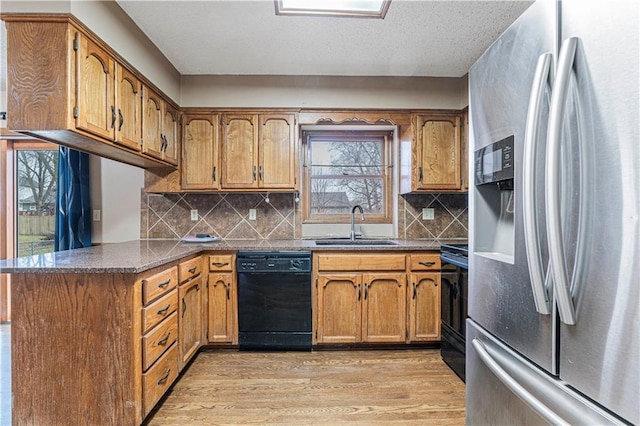 kitchen with sink, light hardwood / wood-style flooring, stainless steel fridge, black dishwasher, and kitchen peninsula