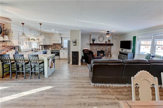 living room featuring ceiling fan, a brick fireplace, a wealth of natural light, and light hardwood / wood-style floors